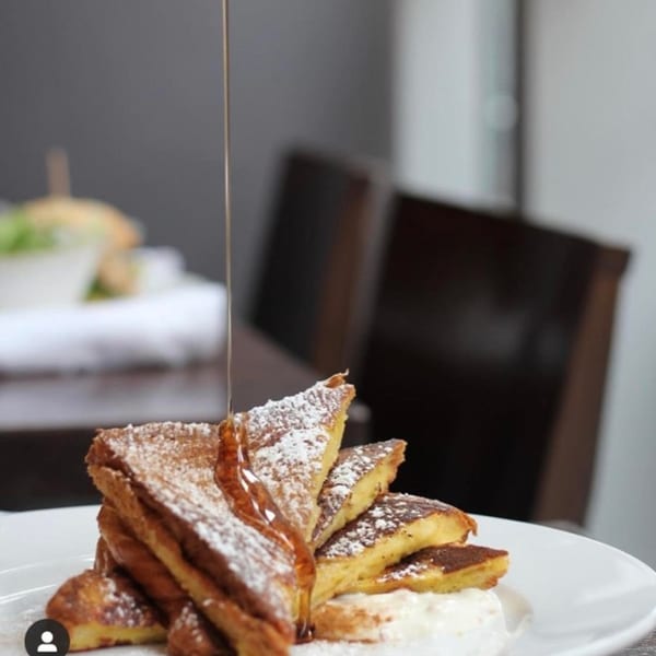 Syrup pouring over a stack of powdered sugar-dusted French toast triangles on a white plate.