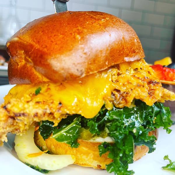 A Kanela Breakfast Club sandwich with fried chicken, melted cheese, and kale on a brioche bun.
