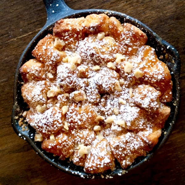 Monkey bread with powdered sugar and nuts in a cast iron skillet on a wooden table.