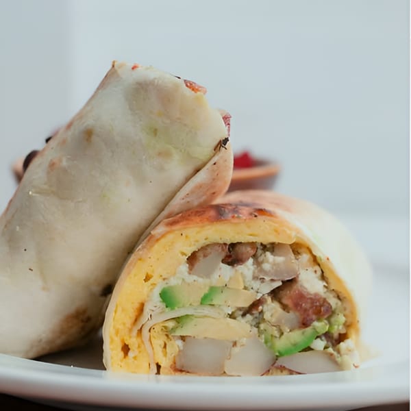 A Kanela Breakfast Club burrito, cut in half, revealing eggs, avocado, potatoes, and bacon.