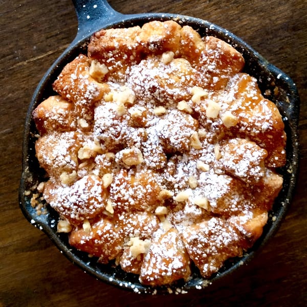 Kanela Breakfast Club's monkey bread, dusted with powdered sugar and chopped nuts, in a cast iron skillet.