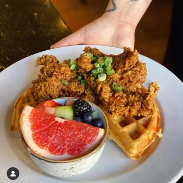 Kanela Breakfast Club's chicken and waffles with a side of fresh fruit, including grapefruit.