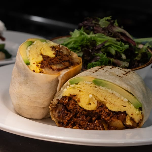 Two halves of a breakfast burrito with eggs, chorizo, and avocado, served with a side salad.