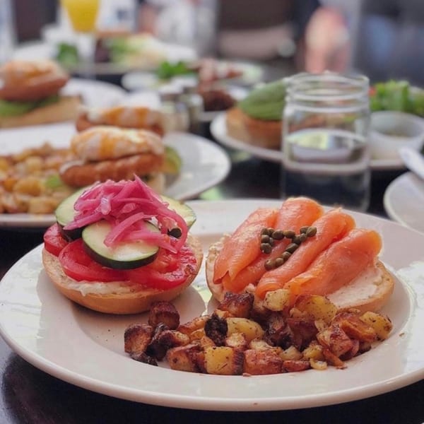 Kanela Breakfast Club's bagel with lox and capers, another with tomatoes and pickled onions, and home fries.
