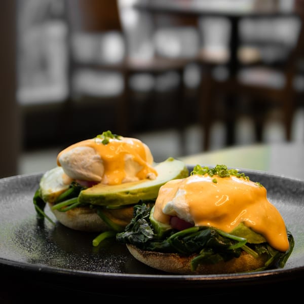 Two Kanela Breakfast Club avocado benedicts with poached eggs, hollandaise, and spinach on a dark plate.